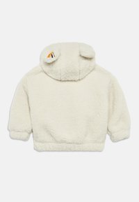 Φλις φούτερ σε κρεμ χρώμα με απαλή υφή, κοντά μανίκια και κουκούλα με μικρές λεπτομέρειες σε σχήμα αυτιών. Ρυθμιζόμενο τελείωμα.