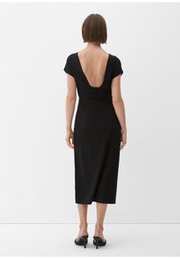 Black midi dress with a deep V-back, fitted bodice, short sleeves, and a smooth texture. Features a concealed zipper at the back.