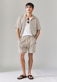 Korte mouwen patroon blouse en bijpassende korte broek in beige tinten, met een trekkoord in de taille, gladde stof en een eenvoudige knoopsluiting.