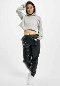 Grå avkortet hettegenser med hette og oransje logo, kombinert med blanke svarte joggebukser med elastisk liv og hvite sneakers.