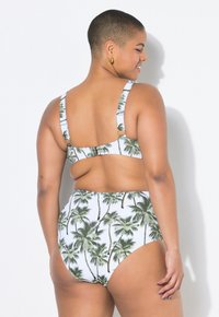 Hooguitgesneden bikini met palmbladprint, voorzien van brede banden en metalen hardware aan de achterkant, in witte en groene kleuren. Glad, rekbaar materiaal.