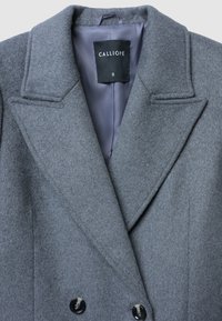 Cappotto doppiopetto grigio in misto lana con ampie rever, due bottoni neri e una fodera grigia liscia. Tag della taglia S visibile.