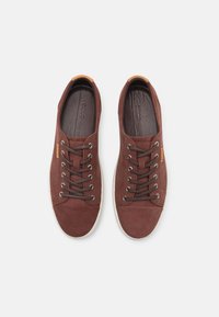 Chaussures décontractées en daim marron avec un bout arrondi, six œillets en métal, des lacets marron et une semelle en caoutchouc blanche contrastante. Présente un accent logotypé.
