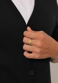 Black cardigan with a v-neck design, button details, and a fitted silhouette. The hand displays a thin gold ring with a circular top.