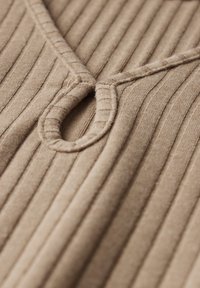 Tessuto a coste beige con scollatura a V e dettaglio a forma di anello circolare al collo. Morbida texture con linee verticali prominenti.