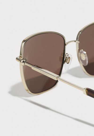 Braun getönte Sonnenbrille mit goldfarbenem Metallrahmen, square Form, klaren Nasenpads und einem markenfähigen Arms mit dunklem Schildpatt-Akzent.