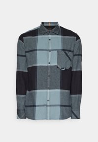 Chemise à manches longues boutonnée avec grand motif à carreaux bleu, gris et noir et poche poitrine à rabat.