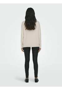 Pull en tricot beige avec ourlet côtelé, associé à un pantalon skinny noir. Le pull présente une coupe décontractée et des manches longues. Des chaussures noires complètent le look.