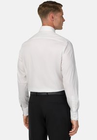 Camicia bianca a maniche lunghe con colletto punta e polsini abbottonati, abbinata a pantaloni neri. Tessuto a finitura liscia e vestibilità classica.
