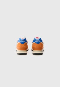 Orange suede sneakers with blue accents, white and red detailing on the heel, and a black rubber sole. "New Balance" logo visible.