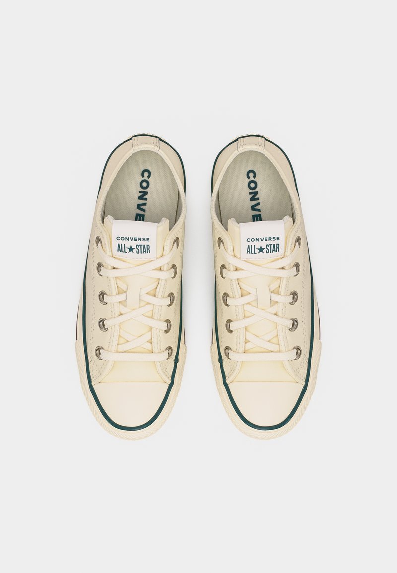 Paar beige Converse All Star Low-Top-Sneaker mit weißen Schnürsenkeln und grünem Rand, von oben auf einem hellen Hintergrund gesehen.