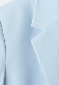 Gros plan sur un tissu bleu clair montrant une texture détaillée à côtes diagonales et des plis nets et superposés.