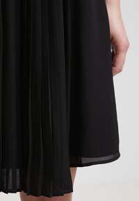 Abito nero a pieghe con un design fluido, realizzato in un tessuto testurizzato e con dettagli trasparenti all'orlo e ai bordi delle pieghe.