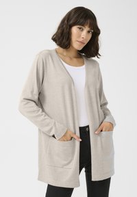 Lichtbeige cardigan met lange mouwen, open voorkant en twee zijzakken. Gemaakt van een zachte stof met een gladde textuur.