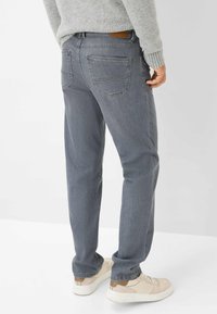 Jeans in denim grigio con una vestibilità comoda, dotati di due tasche posteriori e una patch in pelle marrone sulla vita. Abbinati a sneakers crema.