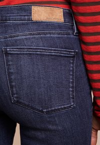 Mörkblå denimjeans med en slät yta, som har en bakficka och en ljusbrun läderetikett med "BOSS ORANGE" präglat.