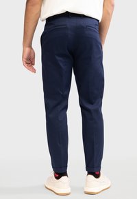 Navy blue trousers with a slim fit and tapered legs. Features side pockets and two back pockets. Worn with white sneakers and patterned socks.