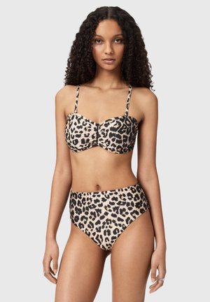 Femme portant un bikini taille haute à imprimé léopard avec un haut froncé, posant devant un fond gris clair uni.