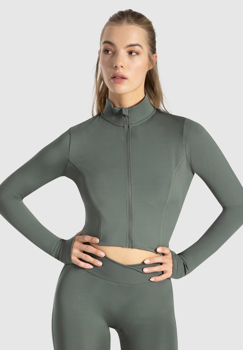 Crop top i afdæmpet grøn stof med høj krave, fuld lynlås, lange ærmer og flade sømme for et rent finish.