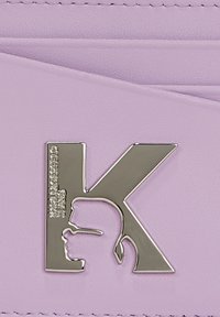 Piele lavandă cu un finisaj texturat. Prezintă un logo argintiu în formă de litera "K" alături de o siluetă de profil.