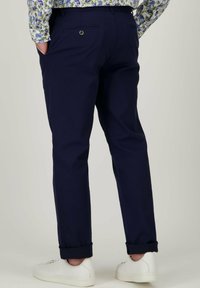 Marineblauwe chino's met een relaxte pasvorm, voorzien van achterzakken en opgerolde manchetten. Gecombineerd met witte sneakers voor een casual uitstraling.
