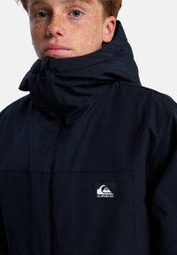 Marineblaue Jacke mit hohem Kragen und Reißverschluss. Verfügt über ein Quiksilver-Logo auf der linken Brust. Glattes Material mit leichtem Design.