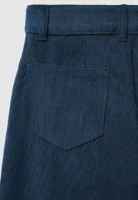 Nahaufnahme von navyblauen Cordhosen, die die Gesäßtasche, den Gürtelschlaufen und die vertikale Rippenstruktur zeigen.