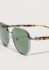 Okulary przeciwsłoneczne o okrągłych zielonych soczewkach, srebrnej metalowej oprawie i zdobieniu w panterkę na zausznikach. Posiadają noski oraz ozdobę z logo.