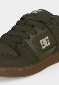 Κοντινό πλάνο ελιάς πράσινου παπουτσιού DC με υφή δέρματος, χονδρά κορδόνια και καφέ λαστιχένια σόλα.