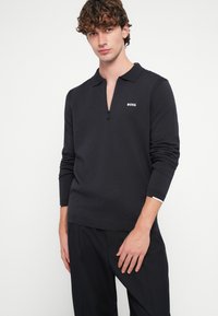 Melnīt pusriteni ar apkakli, kreisajā krūtīs ir balts "BOSS" logotips. Izgatavots no faktūras adīta auduma, pieguļošs dizains.