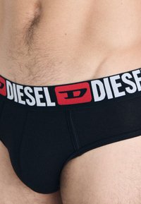 Caleçons en coton noirs avec une large ceinture élastique arborant le logo "DIESEL" en blanc et rouge ainsi qu'un accent logo. Texture lisse.