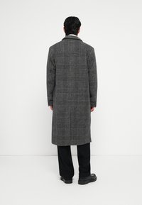 Gray plaid long coat with a collar, textured wool fabric, and loose fit. Paired with black trousers and shoes, viewed from the back.