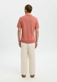 Kortermet polo-sweater med krage i lys korallfarge med strukturert strikk mønster, kombinert med løstsittende, kremfargede linbukser.