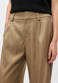 Beżowe, dopasowane spodnie o gładkiej teksturze, z przednimi zakładkami, bocznymi kieszeniami oraz prostym krojem nogawek.