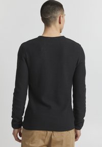 Zwarte lange mouwen trui met een gemêleerd breipatroon, een ronde halslijn en een licht gebogen zoom, gedragen met beige broeken.