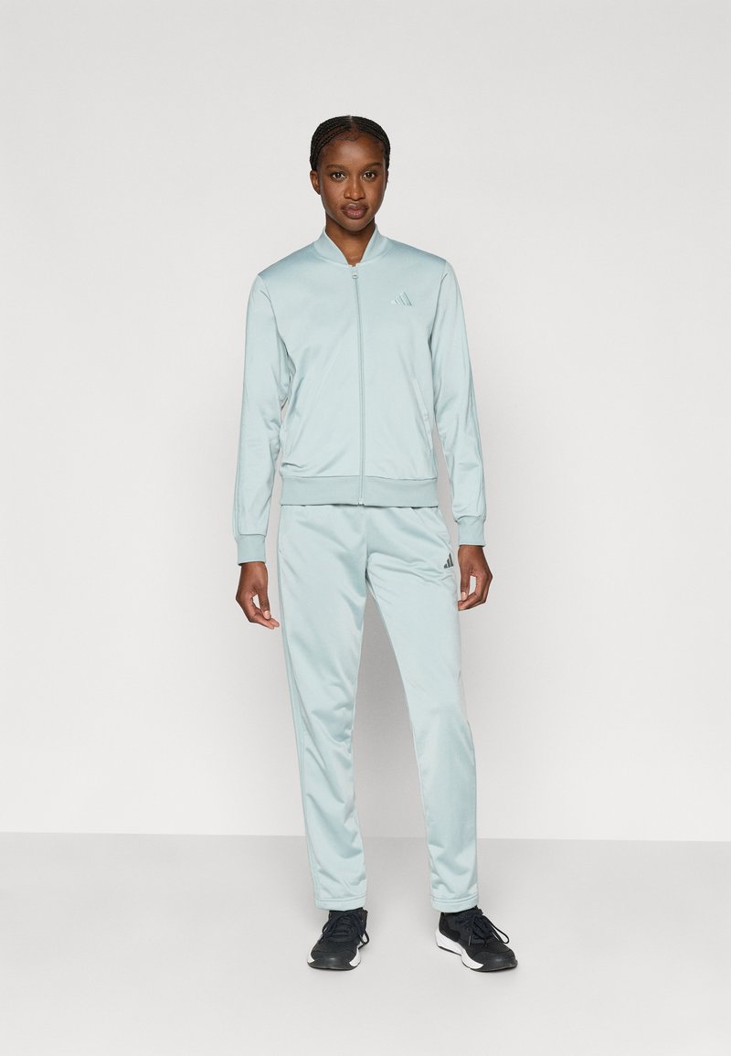 Jasnoniebieski dres wykonany z miękkiego materiału, składający się z bluzy na zamek oraz dopasowanych spodni, z subtelnym logo na bluzie i spodniach.