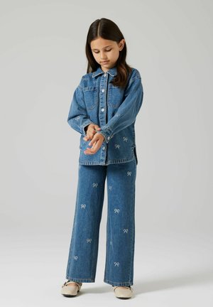 Denimjakke og buksesett i blå vask med hvit sløyfebroderi, avslappet passform, knappelukking og sidesplitter på jakken.