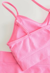 Różowy sportowy crop top z cienkimi ramiączkami, miękkim teksturem materiału i dopasowanym krojem. Posiada gładkie wykończenie i bezszwowy pasek u dołu.