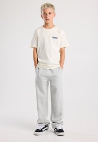 Crewneck t-shirt in off-white with "VENICE" printed in blue, paired with light grey sweatpants and black Vans sneakers. Simple design overall.