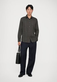 Camisa de manga larga a rayas negras con cierre de botones en la parte delantera, combinada con pantalones de pinstripe en navy y una bolsa cilíndrica negra. Textura suave, corte moderno.