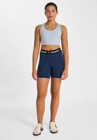 Ljusblå sportbh med rund hals, tillsammans med marinblå högmidjade shorts med en svart midja med logotyp. Sneakers fulländar looken.
