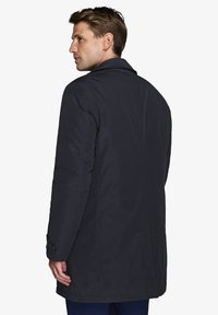 Herre navy blå parka med lige snit, knapmanchetter og en glat, mat overflade. Har en bagsideventil for bedre mobilitet.