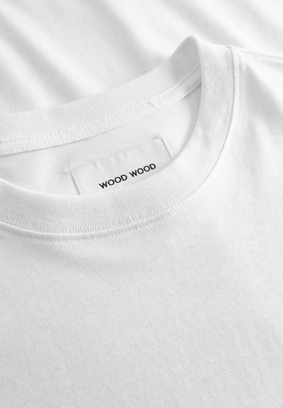 Κοντινή λήψη λευκού T-shirt με στρογγυλή λαιμόκοψη και ορατή ετικέτα στο λαιμό που γράφει "WOOD WOOD."