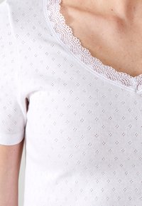 Witte top met korte mouwen en een V-halslijn, voorzien van kantafwerking en een oppervlak met gestructureerde stippen door de stof.