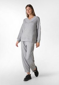 Sudadera gris de gran tamaño con cuello en V y mangas largas, combinada con pantalones de chándal gris de corte holgado. Zapatillas deportivas negras completan el atuendo.