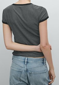 Black and white striped short-sleeve shirt with a round neckline and black trim, paired with light blue denim jeans featuring back pockets.