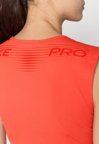 Rød atletisk tank topp med glatt og stretchy stoff. Baksiden har preget "PRO" tekst og subtile horisontale linjer for tekstur.