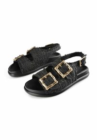 Sandalias negras de tejido con dos grandes hebillas cuadradas en tono dorado y una correa trasera sobre un fondo blanco.