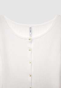 White ribbed top with a rounded neckline, featuring five small beige buttons down the front. Made of textured fabric. Size label visible.