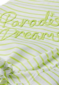 Biely textil s jemne zelenými horizontálnymi pruhmi a vyvýšeným vyšívaným textom "Paradise Dreams" v zodpovedajúcej zelenej priadze.